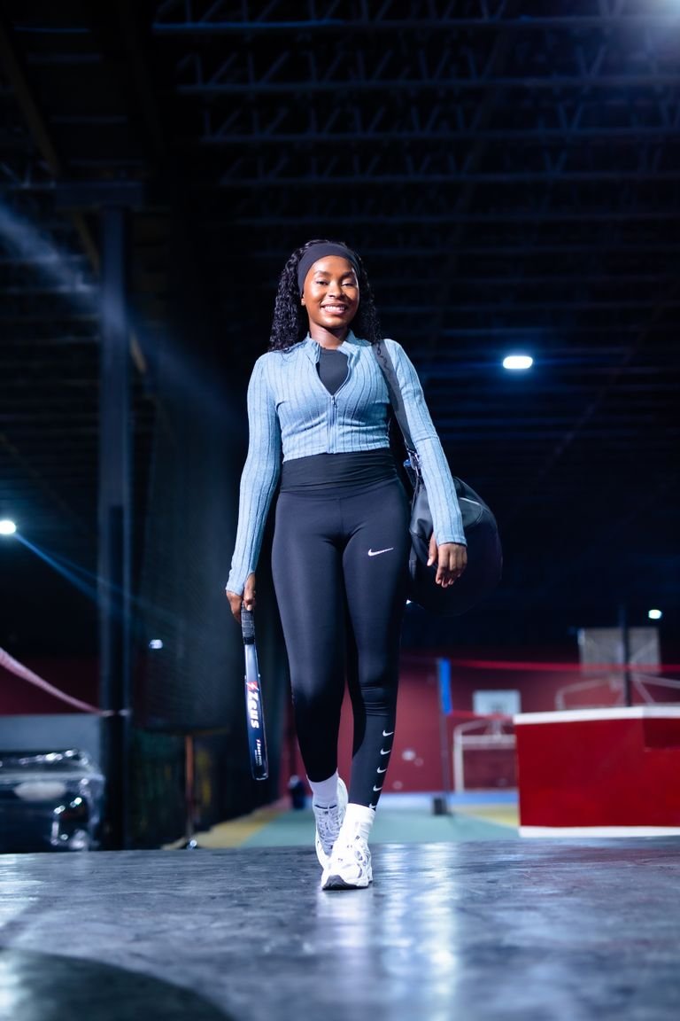 Woman in sportswear holding a racket, walking in an indoor sports venue for padel or tennis.